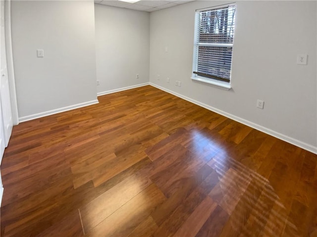 unfurnished room with baseboards, a paneled ceiling, and wood finished floors