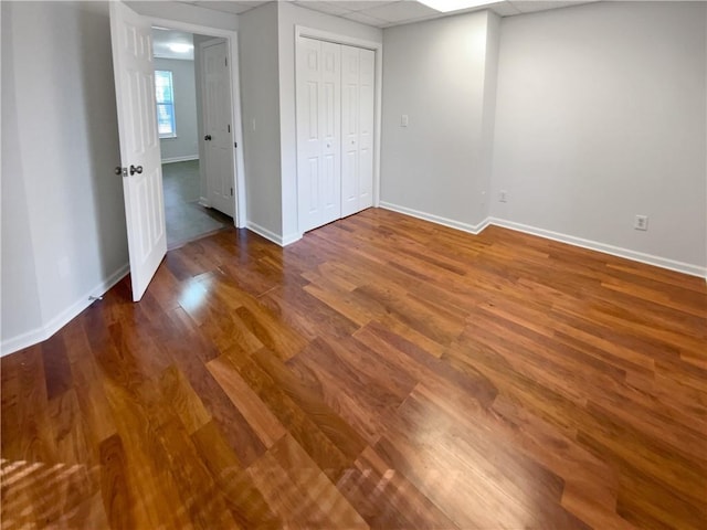 unfurnished bedroom with a closet, a paneled ceiling, baseboards, and wood finished floors