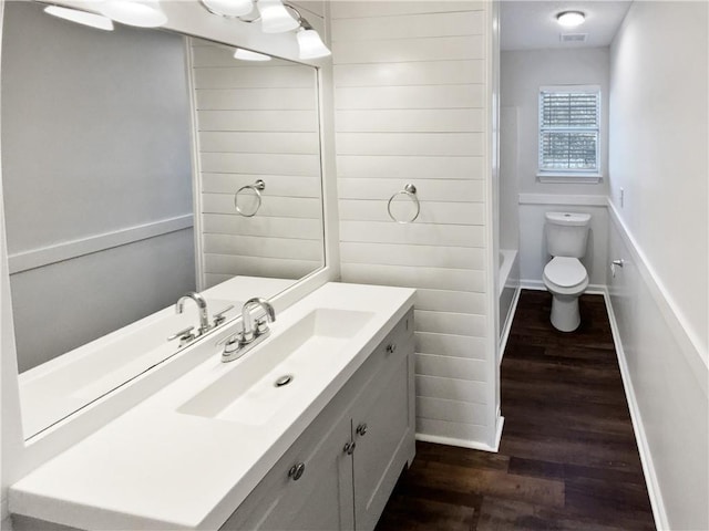 bathroom featuring visible vents, baseboards, toilet, wood finished floors, and vanity