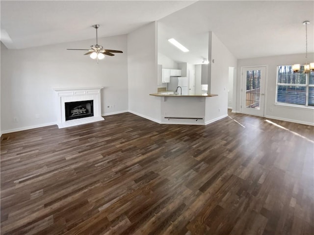 unfurnished living room with lofted ceiling, ceiling fan with notable chandelier, dark wood-type flooring, and a fireplace with raised hearth