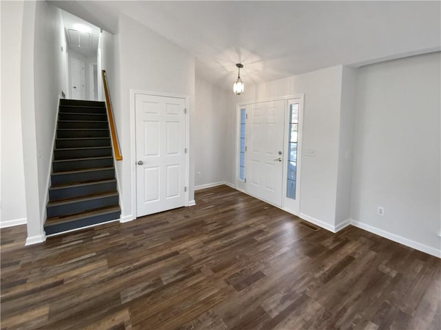 foyer entrance with dark wood finished floors, an inviting chandelier, stairway, and baseboards