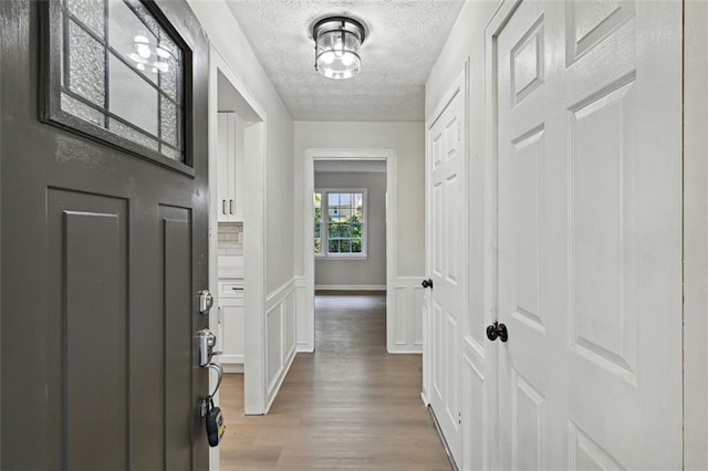 hall with light wood-type flooring and a textured ceiling