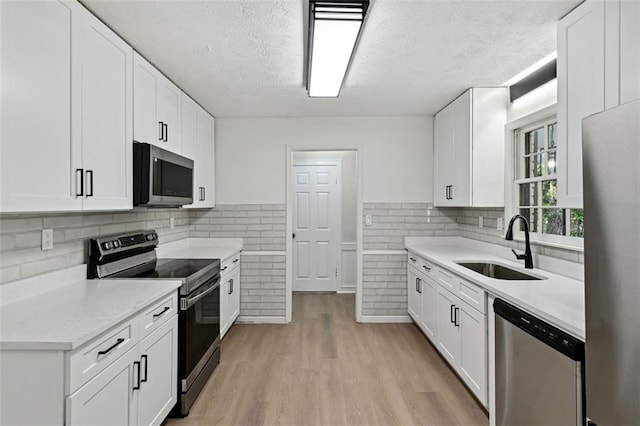 kitchen featuring a textured ceiling, light hardwood / wood-style floors, sink, white cabinetry, and appliances with stainless steel finishes