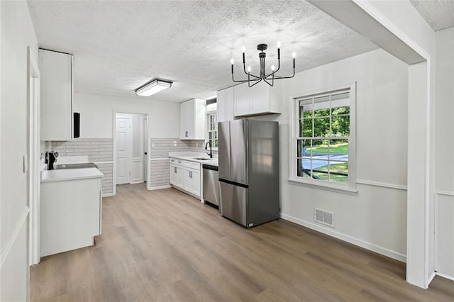 kitchen featuring wood-type flooring, a textured ceiling, white cabinets, stainless steel appliances, and backsplash