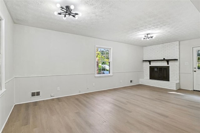 unfurnished living room featuring a brick fireplace, a textured ceiling, a chandelier, and wood-type flooring