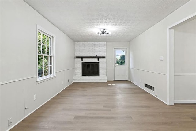 unfurnished living room featuring a brick fireplace, a textured ceiling, and light hardwood / wood-style flooring