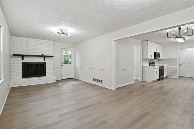 unfurnished living room with a textured ceiling, light hardwood / wood-style floors, and a brick fireplace