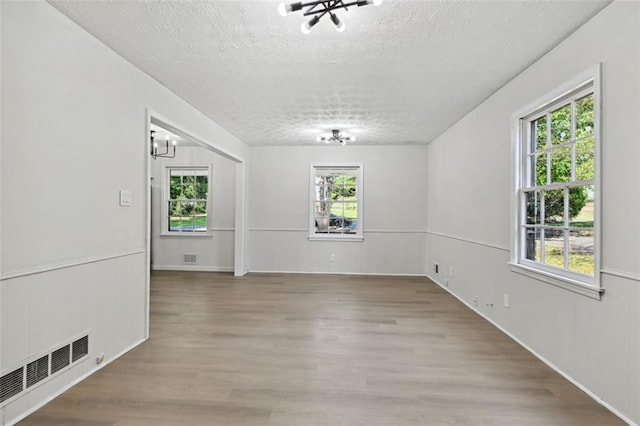 empty room with a textured ceiling, hardwood / wood-style floors, a chandelier, and a wealth of natural light