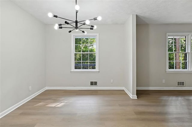 unfurnished room featuring a textured ceiling, plenty of natural light, hardwood / wood-style floors, and a chandelier