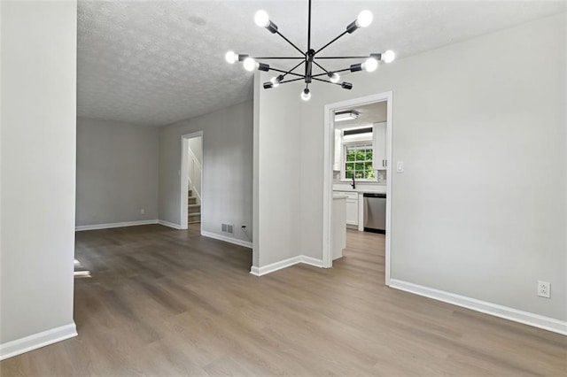 interior space with a textured ceiling, an inviting chandelier, light hardwood / wood-style flooring, and sink