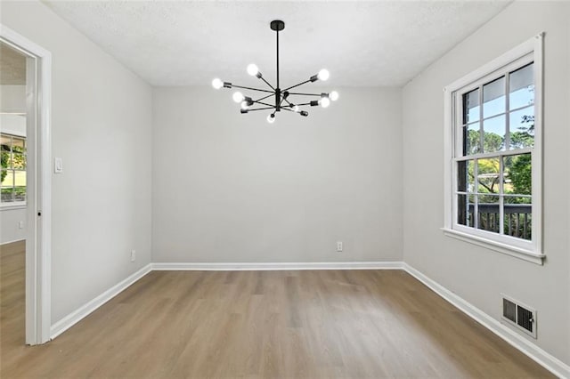 unfurnished room featuring a textured ceiling, light hardwood / wood-style floors, and an inviting chandelier