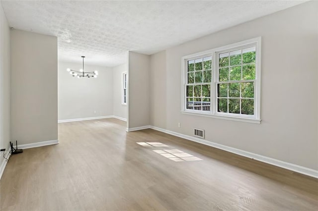 empty room with an inviting chandelier, hardwood / wood-style floors, and a textured ceiling