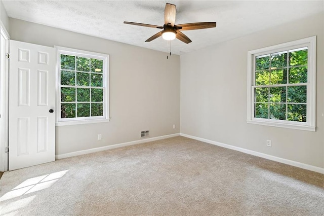 spare room with ceiling fan, light colored carpet, and plenty of natural light