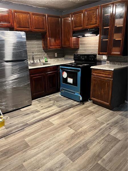 kitchen featuring light countertops, black range with electric stovetop, freestanding refrigerator, a sink, and under cabinet range hood