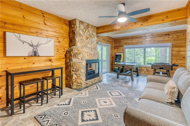 living room with a textured ceiling, beamed ceiling, a ceiling fan, and wooden walls