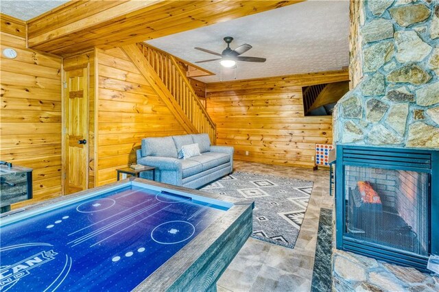 recreation room with a ceiling fan, a fireplace, wooden walls, and a textured ceiling