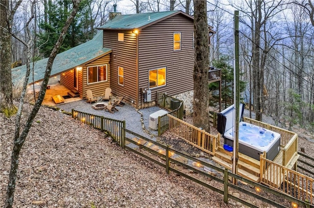 back of property with faux log siding, a jacuzzi, metal roof, gravel driveway, and a wooden deck