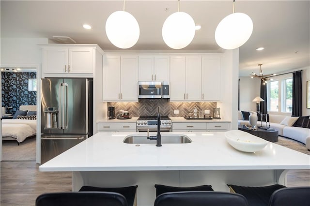 kitchen with high end appliances, pendant lighting, an island with sink, and white cabinets