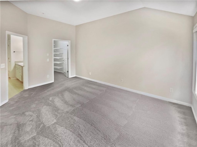 unfurnished bedroom with vaulted ceiling, ensuite bath, a walk in closet, a closet, and carpet flooring