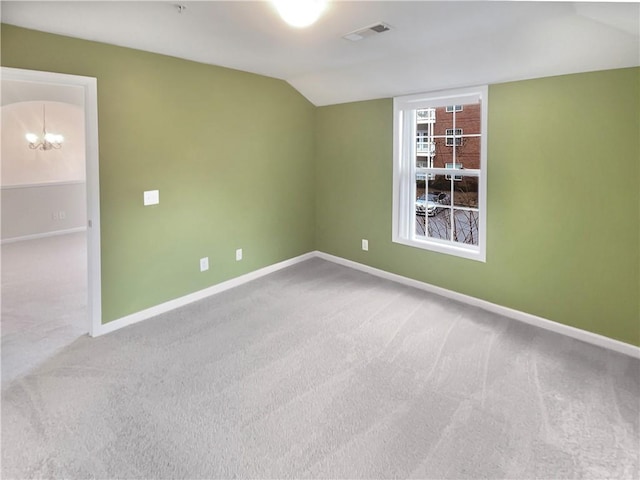 carpeted spare room with an inviting chandelier and vaulted ceiling