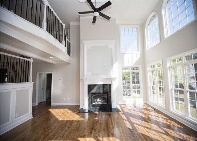 unfurnished living room featuring baseboards, ornamental molding, a ceiling fan, wood finished floors, and a premium fireplace