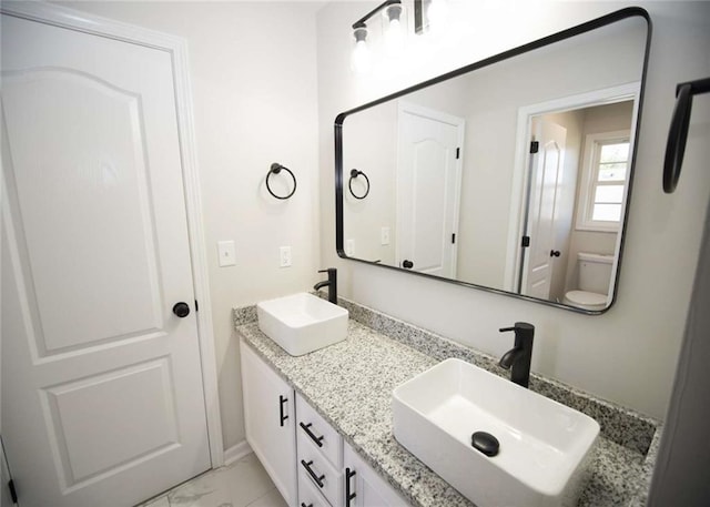 full bath featuring toilet, double vanity, marble finish floor, and a sink
