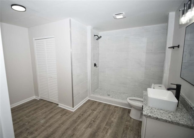bathroom with a tile shower, vanity, toilet, wood finished floors, and baseboards