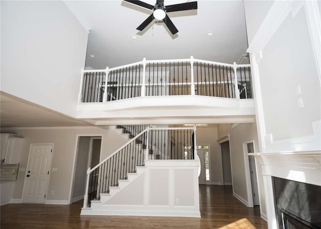 stairs with wood finished floors, a fireplace, a towering ceiling, and a ceiling fan