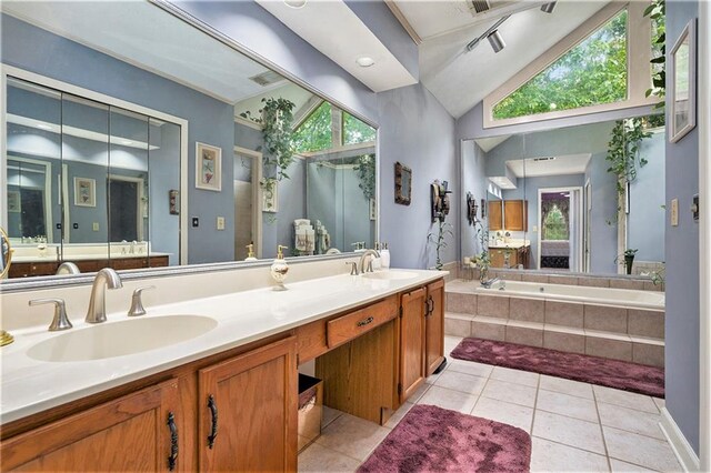 bathroom featuring a wealth of natural light, vanity, tile patterned flooring, and a relaxing tiled tub