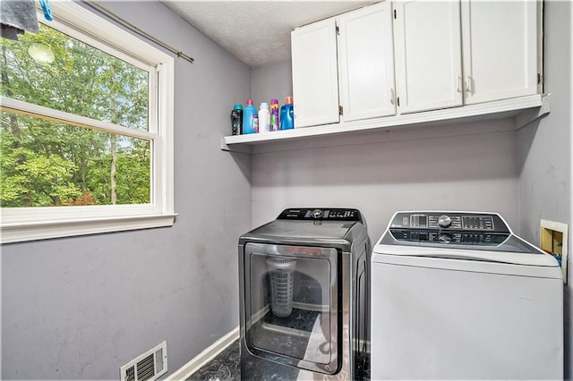 clothes washing area with cabinets, a textured ceiling, and washing machine and dryer