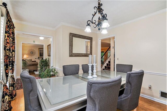 dining area with wood-type flooring, a chandelier, and ornamental molding