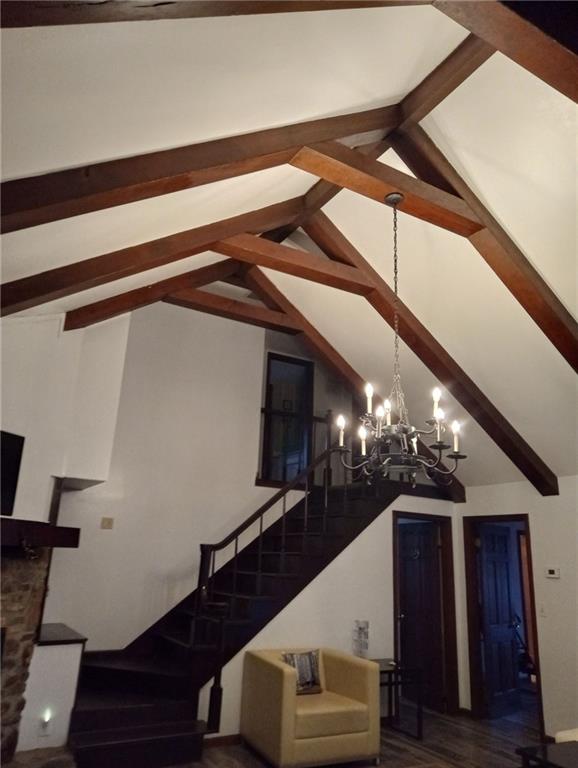 staircase with hardwood / wood-style flooring, a notable chandelier, and vaulted ceiling with beams