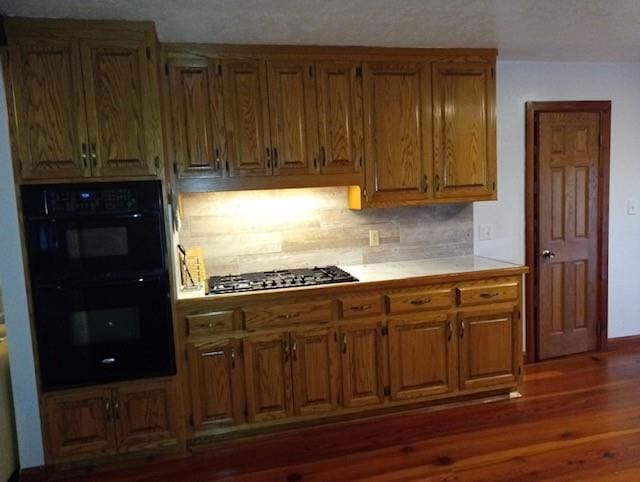 kitchen featuring stainless steel gas stovetop, decorative backsplash, dark hardwood / wood-style flooring, and double oven