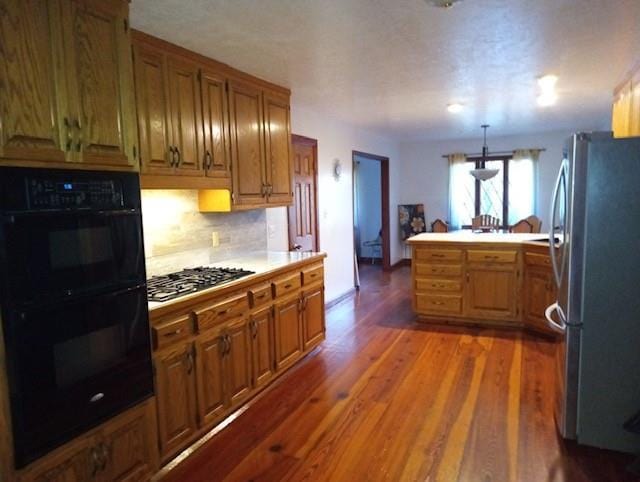 kitchen featuring hanging light fixtures, backsplash, stainless steel appliances, dark hardwood / wood-style flooring, and kitchen peninsula