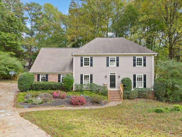 colonial-style house featuring a front lawn and a shingled roof