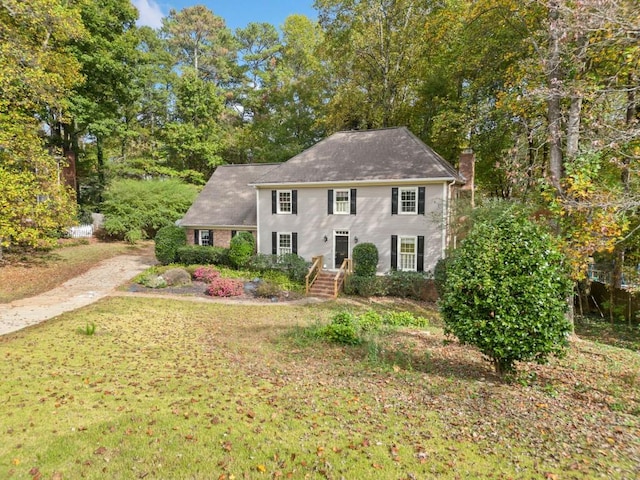 colonial inspired home with driveway, a chimney, and a front lawn