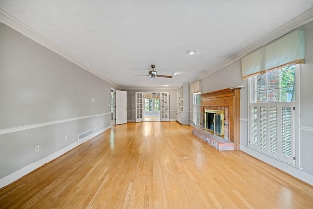 unfurnished living room with visible vents, light wood-style floors, a brick fireplace, and crown molding