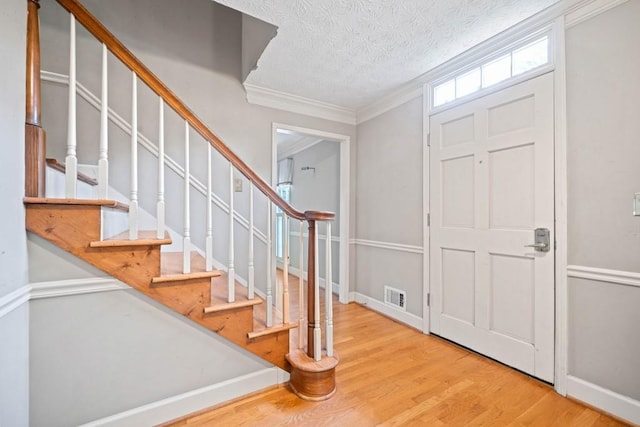 foyer entrance with wood finished floors, baseboards, visible vents, a textured ceiling, and crown molding