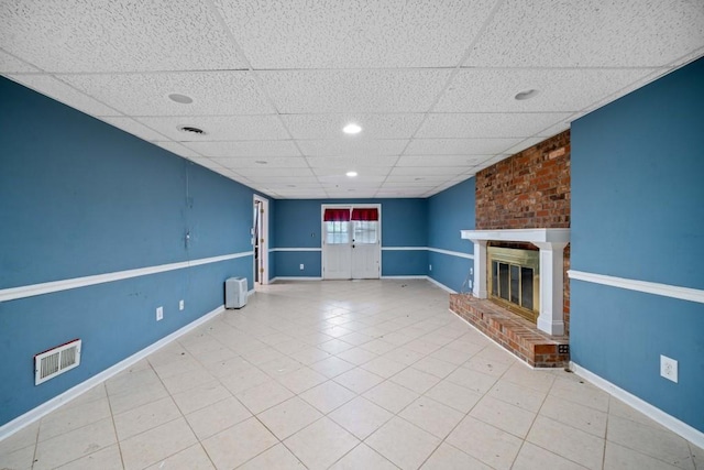 unfurnished living room with visible vents, a brick fireplace, baseboards, and a drop ceiling