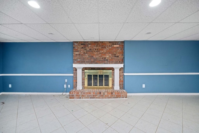 unfurnished living room featuring a drop ceiling, a fireplace, and baseboards