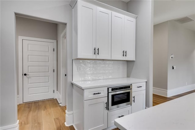 kitchen with light countertops, stainless steel oven, light wood-style flooring, visible vents, and decorative backsplash