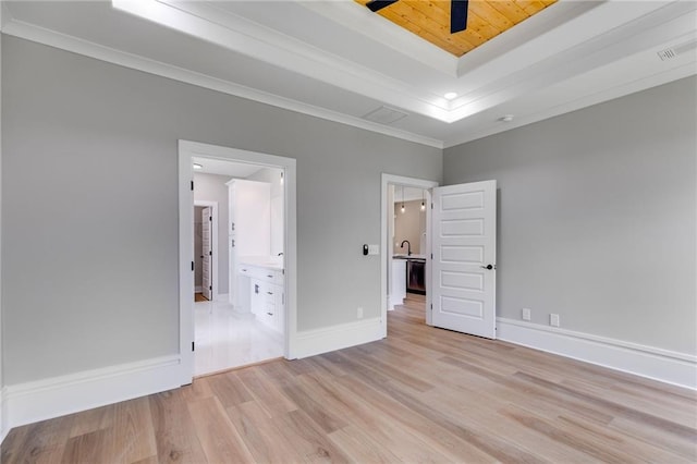 unfurnished bedroom with a raised ceiling, light wood-type flooring, ensuite bathroom, baseboards, and ornamental molding