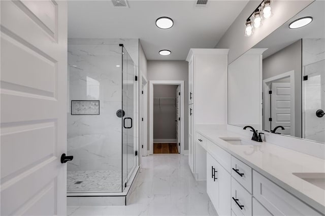 bathroom featuring a walk in closet, a marble finish shower, marble finish floor, a sink, and double vanity