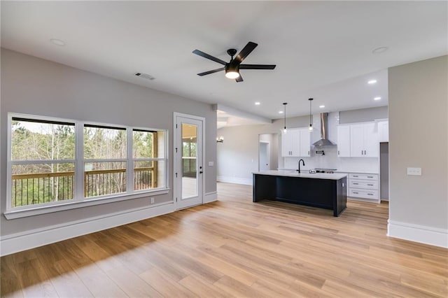 kitchen featuring light countertops, a ceiling fan, wall chimney range hood, visible vents, and light wood-style floors