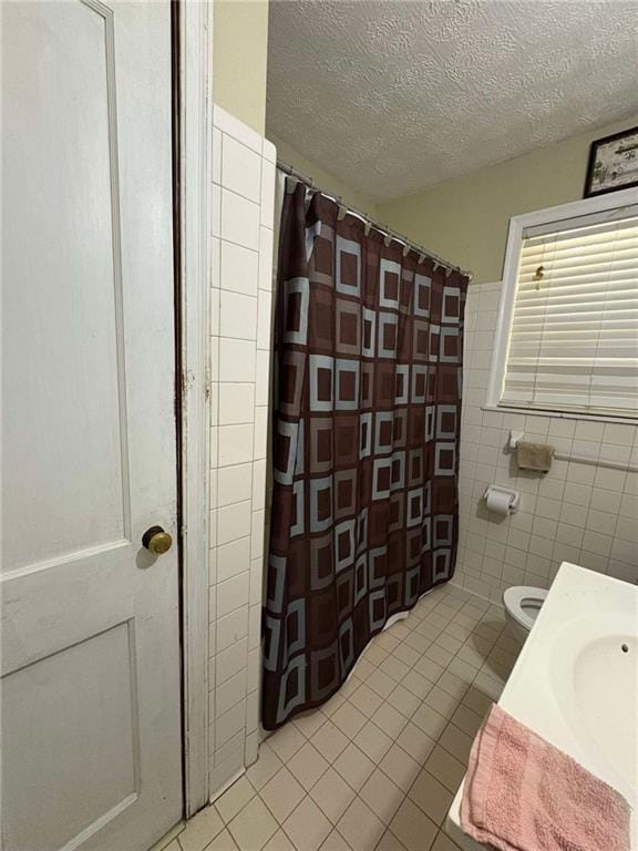 bathroom with tile walls, tile patterned flooring, toilet, and a textured ceiling