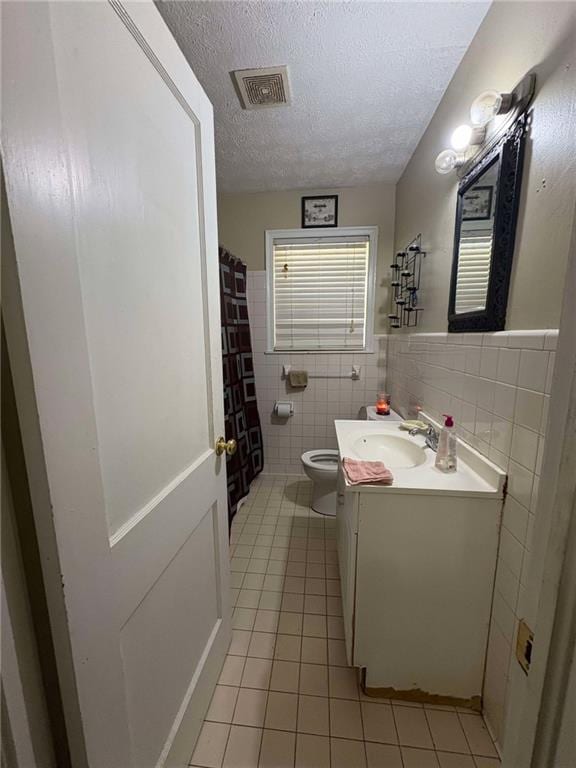 bathroom with a textured ceiling, tile walls, toilet, tile patterned floors, and vanity