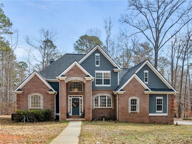 view of front of home featuring roof with shingles, a front yard, and brick siding