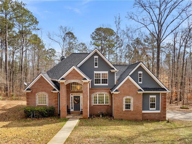 view of front of home featuring brick siding, roof with shingles, and a front yard