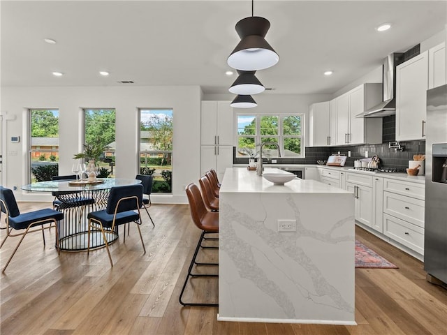 kitchen featuring tasteful backsplash, white cabinetry, light wood-style floors, and wall chimney range hood