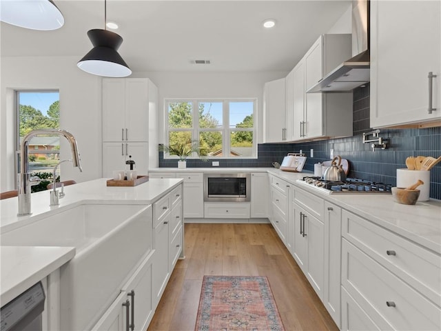 kitchen with backsplash, appliances with stainless steel finishes, light wood-style floors, a sink, and wall chimney exhaust hood